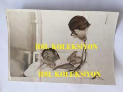 EFSANE MÜZİK GRUBU BEYAZ KELEBEKLER'İN ÇOK NADİR BİR ORİJİNAL FOTOĞRAFI, 18 x 12 cm EBADINDA, SİYAH & BEYAZ - BEYAZ KELEBEKLER'İN KAZADA YAŞAMINI YİTİREN KARDEŞLERDEN RIFAT EKE'NİN KAZA ÖNCESİNDE HASTANEDE TEDAVİ EDİLDİĞİ VE DOKTOR MUAYENESİ GÖRDÜĞÜ BİR DÖNEMDEN KARE, 1960'LAR