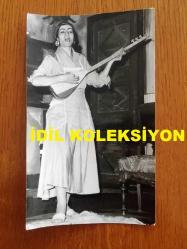 NEJAT UYGUR'UN EŞİ NECLA UYGUR'UN ORİJİNAL FOTOĞRAFI - 16 x 9,5 cm EBADINDA - SİYAH & BEYAZ - NECLA UYGUR BİR TİYATRO OYUNU SIRASINDA SAZ ÇALIP TÜRKÜ SÖYLERKEN ÇEKİLMİŞ BİR KARE