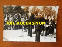 TÜRK HALK MÜZİĞİ SANATÇISI HASAN MUTLUCAN'IN ORİJİNAL FOTOĞRAFI - 18 x 12 cm EBADINDA - HASAN MUTLUCAN HALKA AÇIK SAHNEDE KORO ve SAZCI ÖNÜNDE TÜRKÜ SÖYLERKEN ÇEKİLMİŞ BİR KARE