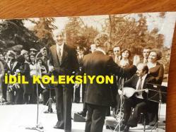 TÜRK HALK MÜZİĞİ SANATÇISI HASAN MUTLUCAN'IN ORİJİNAL FOTOĞRAFI - 18 x 12 cm EBADINDA - HASAN MUTLUCAN HALKA AÇIK SAHNEDE KORO ve SAZCI ÖNÜNDE TÜRKÜ SÖYLERKEN ÇEKİLMİŞ BİR KARE