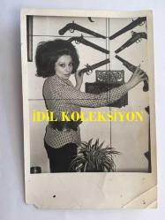 YEŞİLÇAM'IN EFSANESİ BELGİN DORUK'UN ORİJİNAL FOTOĞRAFI, 18 x 12 cm EBADINDA - BELGİN DORUK EVİNDE DUVARA ASILI OLAN ANTİKA TABANCALARI GÖSTERİRKEN ÇEKİLMİŞ BİR FOTOĞRAF