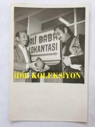 YILDIRIM GENCER'İN ORİJİNAL 2'Lİ FOTOĞRAF SETİ 18 x 12 cm EBADINDA - YILDIRIM GENCER ve ÜLKÜ ÖZEN BİRLİKTE ROL ALDIKLARI ''ŞAFAKTA SİLAH SESLERİ (1973'' İSİMLİ FİLM SONRASI ARMUT HEDİYE EDİLİRKEN ÇEKİLMİŞ 2 FARKLI KARE (ALİ BABA LOKANTASI TABELASI)