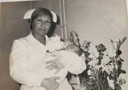 Çicekleri arkasında alıp yeni doğmuş bir bebeği kucağın alarak poz veren yetişkin bir hemşirenin fotoğrafı.ORJİNAL SİYAH & BEYAZ 17x12cm EBADINDA - 1940'LAR, 1950'LER, 1960'LAR ve 1970'LER