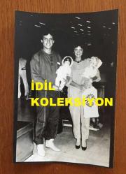 ŞARKICI NECO'NUN ORİJİNAL 2'Lİ FOTOĞRAF SETİ 18 x 12 cm EBADINDA - NECO, EŞİ OYA GERMEN'LE AVRUPA'DAN 15 GÜNLÜK TATİLDEN DÖNDÜKLERİNDE KUCAKLARINDA TUTTUKLARI 2 OYUNCAK BEBEKLE HAVA LİMANINDA POZ VERİRKEN ÇEKİLMİŞ 2 FARKLI KARE, 1984