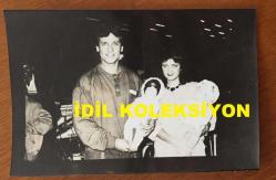 ŞARKICI NECO'NUN ORİJİNAL 2'Lİ FOTOĞRAF SETİ 18 x 12 cm EBADINDA - NECO, EŞİ OYA GERMEN'LE AVRUPA'DAN 15 GÜNLÜK TATİLDEN DÖNDÜKLERİNDE KUCAKLARINDA TUTTUKLARI 2 OYUNCAK BEBEKLE HAVA LİMANINDA POZ VERİRKEN ÇEKİLMİŞ 2 FARKLI KARE, 1984