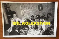 YILMAZ GÜNEY ve YEŞİLÇAM'IN YILDIZI FATMA GİRİK'İN ORİJİNAL FOTOĞRAFI - 18 x 12 cm EBADINDA - ŞARKI SÖYLEYEN FATMA GİRİK MEKANA KONUK OLARAK GELEN YILMAZ GÜNEY ve FATOŞ GÜNEY'İN MASASINA GELİP ÇİÇEK UZATIRKEN ÇEKİLMİŞ ÇOK ÖZEL BİR KARE