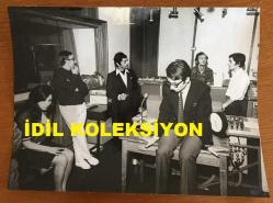 TÜLAY GERMAN'IN ORİJİNAL BÜYÜK BOY FOTOĞRAFI - 27 x 20 cm EBADINDA (AÇIKLAMAYI OKUYUNUZ) - TÜLAY GERMAN STÜDYODA OTURUP BEKLERKEN ÇEKİLMİŞ BİR KARE, STÜDYODAKİ EKİP ARKADAŞLARI ve PLAKLAR AYNI KAREDE