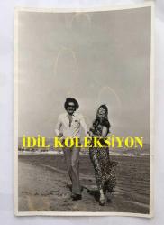 FERİ CANSEL'İN ORİJİNAL FOTOĞRAFI - 18 x 12 cm EBADINDA - FERİ CANSEL SEVGİLİSİYLE DENİZ KENARINDA YÜRÜYÜP GÜLÜŞÜRKEN ÇEKİLMİŞ BİR KARE