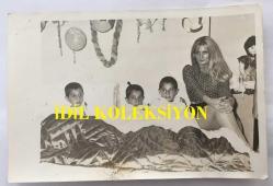 DANSÖZ ve OYUNCU ÖZCAN TEKGÜL'ÜN ORİJİNAL FOTOĞRAFI - 18 x 12 cm EBADINDA - ÖZCAN TEKGÜL SÜNNET OLAN ÇOCUKLARIN YANINDA OTURURKEN ÇEKİLMİŞ BİR HATIRA FOTOĞRAFI, 17 HAZİRAN 1980 (KÜLTÜR BAKANI TEVFİK KORALTAN, ÖZCAN TEKGÜL'E ONUR BELGESİ VERECEK)