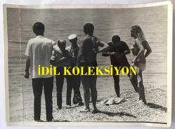 DANSÖZ ve OYUNCU ÖZCAN TEKGÜL'ÜN ORİJİNAL BÜYÜK BOY FOTOĞRAFI - 24 x 18 cm EBADINDA - ÖZCAN TEKGÜL DENİZ KENARINDA ÜSTSÜZ OLARAK ÇEKİM YAPTIRIRKEN ÇEKİLMİŞ BİR KARE