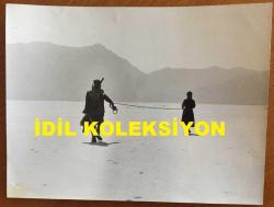 HAYATİ HAMZAOĞLU'NUN ORİJİNAL BÜYÜK BOY FOTOĞRAFI  - 24 x 18 cm EBADINDA - HAYATİ HAMZAOĞLU BİR YEŞİLÇAM FİLMİ SAHNESİNDE ARAZİDE BİR KIZI İPLE YÜRÜTÜRKEN ÇEKİLMİŞ BİR KARE