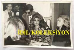 TÜRK SANAT MÜZİĞİ SANATÇISI SEVİM TUNA'NIN ORİJİNAL 2'Lİ FOTOĞRAF SETİ - 18 x 12 cm EBADINDA - SEVİM TUNA, SERPİL ÖRÜMCER'LE BİRLİKTE BERKANT'I DÜĞÜNÜNDE TEBRİK ETMEK İÇİN KOLTUK DEĞNEKLERİYLE GİDERKEN ÇEKİLMİŞ 2 FARKLI KARE