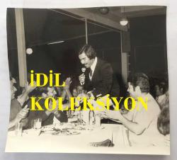 NURİ SESİGÜZEL'İN ORİJİNAL 2'Lİ FOTOĞRAF SETİ - 16 x 14 cm EBADINDA  - NURİ SESİGÜZEL BİR MEKANDA MÜŞTERİLERİN MASASINA GELİP ŞARKI OKURKEN ÇEKİLMİŞ 2 FARKLI FOTOĞRAF