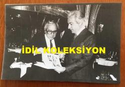 VAKKO'NUN KURUCUSU VİTALİ HAKKO'NUN ORİJİNAL AJANS-BASIN FOTOĞRAFI (KAĞIT BASKI) - 18 x 12 cm EBADINDA - VİTALİ HAKKO, VAKKO'NUN İNGİLTERE'DE LONDRA REGINE KULÜP'TE VERDİĞİ DEFİLEDE TÜRK BAŞKONSOLOSU YÜKSEL SÖYLEMEZOĞLU'NA GİYSİ KATALOĞUNU GÖSTERİRKEN ÇEKİLMİŞ BİR KARE, 5 NİSAN 1979