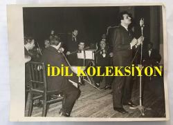 KLASİK TÜRK MÜZİĞİ SANATÇISI ve BESTECİ YILDIRIM GÜRSES'İN ORİJİNAL BÜYÜK BOY FOTOĞRAFI - 24 x 18 cm EBADINDA - YILDIRIM GÜRSES'İN 1960'LARDA ORKESTRANIN ÖNÜNDE '''GENÇLİĞE VEDA'' ŞARKISINI OKURKEN ÇEKİLMİŞ NET KALİTEDE BİR FOTOĞRAFI