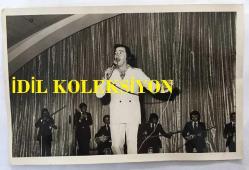 TÜRK HALK MÜZİĞİ SANATÇISI AHMET SEZGİN'İN ORİJİNAL FOTOĞRAFI - 18 x 12 cm EBADINDA - AHMET SEZGİN SAHNEDE SAZCILARIN ÖNÜNDE TÜRKÜ OKURKEN ÇEKİLMİŞ BİR KARE