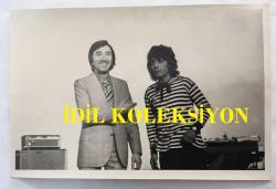 NEJAT UYGUR ve TÜRK HALK MÜZİĞİ SANATÇISI AHMET SEZGİN'İN ORİJİNAL FOTOĞRAFI - 18 x 12 cm EBADINDA - AHMET SEZGİN ve NEJAT UYGUR BİRLİKTE SAHNEDELERKEN ÇEKİLMİŞ BİR FOTOĞRAF