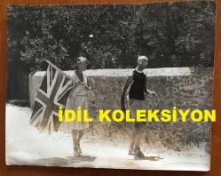 KIBRIS BARIŞ HAREKATI SÜRECİNDE KIBRIS'TAN ÇIKARILAN İNGİLİZ ve DİĞER YABANCI TURİSTLERİN ORİJİNAL BÜYÜK BOY AJANS-BASIN FOTOĞRAFI - 24 x 19 cm EBADINDA - (AÇIKLAMAYI OKUYUNUZ) - 1974 - SAVAŞ SIRASINDA BÖLGEDE MAHSUR EVELYN CHAVASSE ve EŞİ EDITH CHAVASE, ELLERİNDE İNGİLTERE BAYRAĞI İLE YÜRÜRLERKEN