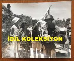 KIBRIS BARIŞ HAREKATI SÜRECİNDE KIBRIS'TAN ÇIKARILAN İNGİLİZ ve DİĞER YABANCI TURİSTLERİN ORİJİNAL BÜYÜK BOY AJANS-BASIN FOTOĞRAFI - 24 x 19 cm EBADINDA - (AÇIKLAMAYI OKUYUNUZ) - 1974 - SAVAŞ SIRASINDA BÖLGEDE MAHSUR EVELYN CHAVASSE ve EŞİ EDITH CHAVASE, ELLERİNDE İNGİLTERE BAYRAĞI ve YANLARINA GELEN ASKERİN KUCAĞINDA TUTTUĞU BEBEKLE HATIRA POZU VERİRLERKEN