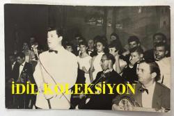 TÜRK SANAT MÜZİĞİ SANATÇISI ve BESTEKAR ARİF SAMİ TOKER'İN ORİJİNAL FOTOĞRAFI - 13,5 x 9 cm EBADINDA - ARİF SAMİ TOKER 1946'DA SAHNE ALDIĞI MEKANDA SAZCILARIN ÖNÜNDE ŞARKISINI OKURKEN ÇEKİLMİŞ BİR KARE