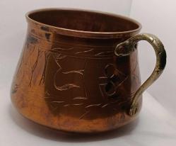 Üzerinde elle yapılmış işlemeler olan pirinç saplı bakır kap