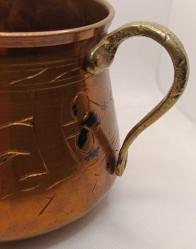 Üzerinde elle yapılmış işlemeler olan pirinç saplı bakır kap