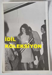 YEŞİLÇAM'IN YILDIZI HÜLYA KOÇYİĞİT'İN ORİJİNAL FOTOĞRAFI  - 18 x 12 cm EBADINDA - HÜLYA KOÇYİĞİT KENDİSİNE VERİLEN ÇİÇEKLE HAYRANLARININ ARASINDA GÜLÜMSERKEN ÇEKİLMİŞ BİR KARE