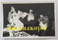 TÜRK HALK MÜZİĞİ SANATÇISI HÜLYA SÜER'İN ORİJİNAL FOTOĞRAFI - 18 x 12 cm EBADINDA - HÜLYA SÜER DİNLEYİCİ MASALARINA GELİP ŞARKI OKURKEN ÇEKİLMİŞ BİR KARE. 23 ŞUBAT 1985