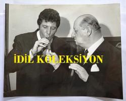 TOM JONES'UN ORİJİNAL BÜYÜK BOY FOTOĞRAFI, İNGİLTERE LONDRA AJANS BASKISI - ORIGINAL PHOTO OF TOM JONES - 22 x 18 cm EBADINDA - TOM JONES, ÜNLÜ MEDYA PATRONU LEW GRADE İLE PURO İÇERKEN ÇEKİLMİŞ ÖZEL BİR KARE (AN ORIGINAL PHOTOGRAPH OF LEW GRADE LIGHTING TOM JONES' CIGAR.) İNGİLİZCE HABER METİNLİ.  1968. ÖZEL ARŞİV!