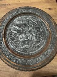 bu tabak, üzerindeki detaylı figürlerle yüksek dekoratif değere sahiptir. Hem koleksiyonluk hem de şık bir duvar aksesuarı arayanlar için kaçırılmayacak bir parçadır. Orta bölümde at üzerinde kılıçlı süvari ve av sahnesi detaylı kabartma (repousse) tekniğiyle işlenmiştir. Tabağın bordür kısmı stilize çiçek ve bitki motifleriyle bezelidir. Bakır üzerine kalay kaplama olup, zamanla oluşan doğal patini sayesinde otantik bir görünüm kazanmıştır. Arkasındaki askı halkası sayesinde duvar dekoru olarak kullanılabilir; şark köşeleri, ofisler veya salonlar için uygundur