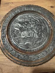 bu tabak, üzerindeki detaylı figürlerle yüksek dekoratif değere sahiptir. Hem koleksiyonluk hem de şık bir duvar aksesuarı arayanlar için kaçırılmayacak bir parçadır. Orta bölümde at üzerinde kılıçlı süvari ve av sahnesi detaylı kabartma (repousse) tekniğiyle işlenmiştir. Tabağın bordür kısmı stilize çiçek ve bitki motifleriyle bezelidir. Bakır üzerine kalay kaplama olup, zamanla oluşan doğal patini sayesinde otantik bir görünüm kazanmıştır. Arkasındaki askı halkası sayesinde duvar dekoru olarak kullanılabilir; şark köşeleri, ofisler veya salonlar için uygundur