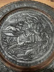 bu tabak, üzerindeki detaylı figürlerle yüksek dekoratif değere sahiptir. Hem koleksiyonluk hem de şık bir duvar aksesuarı arayanlar için kaçırılmayacak bir parçadır. Orta bölümde at üzerinde kılıçlı süvari ve av sahnesi detaylı kabartma (repousse) tekniğiyle işlenmiştir. Tabağın bordür kısmı stilize çiçek ve bitki motifleriyle bezelidir. Bakır üzerine kalay kaplama olup, zamanla oluşan doğal patini sayesinde otantik bir görünüm kazanmıştır. Arkasındaki askı halkası sayesinde duvar dekoru olarak kullanılabilir; şark köşeleri, ofisler veya salonlar için uygundur