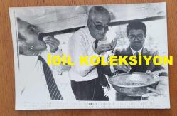 TÜRKİYE CUMHURİYETİ'NİN 8. CUMHURBAŞKANI TURGUT ÖZAL ve ESKİ DIŞİŞLERİ BAKANI VAHİT HALEFOĞLU'NUN ORİJİNAL AJANS-BASIN FOTOĞRAFI - 18 x 12 cm EBADINDA - TURGUT ÖZAL ve VAHİT HALEFOĞLU, GİTTİKLERİ BİR ANADOLU KÖYÜNDE KADINLARIN İKRAM ETTİKLERİ TEPSİDEN HEDİK YERLERKEN ÇEKİLMİŞ BİR KARE