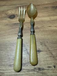 Antika Gümüş İşlemeli Boynuz Servis Takımı Zarafeti ve doğallığı bir arada sunan, koleksiyonluk servis seti (kaşık ve çatal). Özel gün sofralarınıza prestij katacak ya da dekoratif olarak sergilenecek nadide bir parçadır. Tutma yerleri ve uç kısımları doğal boynuz/kemik dokulu özel malzeme. Orta kısımları ince işçilikli, gümüş kaplama kabartma motiflerle bezelidir. Yaşına bağlı hafif bir patina (eskimiş doku) almış olup, herhangi bir kırığı bulunmamaktadır. Vintage/Antika severler için idealdir. Salata servisi veya dekoratif amaçlı uygundur.