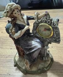 Antika Görünümlü Klasik Kadın Figürlü Masa Saati Zarif kadın figürü ve barok tarzı detaylarla süslenmiş, estetik bir dekoratif objedir. Temiz kullanılmış, vintage bir görünüme sahiptir. Hem saat hem de biblo olarak kullanılabilir. Çalışma masası, konsol üzeri veya kitaplık için mükemmel bir aksesuardır. Şık bir hediye seçeneği olabilir. Poliresin/Döküm benzeri dayanıklı malzeme. Çalışır durumda. 19x 14 cm