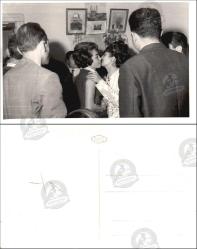 Ev İçi Mekân, Fotoğraf, 1950’ler: Duvarlarda portreler ve harita bulunan bir odada, kalabalık içinde iki kadının selamlaştığı gündelik bir an.