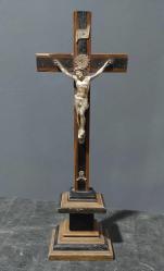 Avrupa, Kaideli İsa Temalı Haç. Kahverengi-Siyah, Üç Katlı, Kısmen Yivli Bir Kaide Üzerinde Duran Bir Haç (Çarmıh). Gövdesi Nikel Gümüşünden Yapılmıştır. Kolları Çapraz Olarak Yukarı Doğru Uzanmaktadır. Gövde, Yukarı Doğru Uzanan Ellerden Geçirilen İki Çivi İle Haçın Enine Kirişine Tutturulmuştur. İki Ayak, Bir Kaide Üzerinde Üst Üste Durmaktadır. Her İki Ayaktan Geçen Çivi Belirtilmiştir. İsa'nın Başının Arkasında/Üstünde Bir Hale (Alev) Bulunmaktadır. Bunun Üzerinde, Kavisli Bir Bant Şeklinde Titulus Crucis (INRI Levhası) Yer Almaktadır. Ayakların Altına, Kemiklerinin Sağ Yarısı Eksik Olan Adem'i Tasvir Eden Metal Bir Kafatası İliştirilmiştir. Bu Siyah Lake Kaplı Ahşap Haçlar Muhtemelen Dini Törenlerde Kullanılmıştır. 1900 Ortaları.