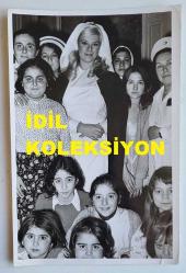 YEŞİLÇAM'IN YILDIZI HÜLYA KOÇYİĞİT'İN ORİJİNAL AJANS-BASIN FOTOĞRAFI - 18 x 12 cm EBADINDA - HÜLYA KOÇYİĞİT, HEMŞİRE GİYSİLERİ GİYİP HAYRANLARININ ARASINDA HATIRA POZU VERİRKEN ÇEKİLMİŞ NET KALİTEDE BİR FOTOĞRAF