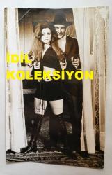 ORHAN GÜNŞİRAY'IN ORİJİNAL FOTOĞRAFI - 18 x 12 cm EBADINDA - ORHAN GÜNŞİRAY, 1970'LERDE BİR FİLM SAHNESİNDE KADIN AKTRİS İLE POZ VERİRKEN ÇEKİLMİŞ BİR KARE