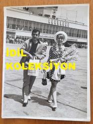 YEŞİLÇAM'IN YILDIZI HÜLYA KOÇYİĞİT'İN ORİJİNAL BÜYÜK BOY FOTOĞRAFI - 24 x 18 cm EBADINDA - HÜLYA KOÇYİĞİT ve EŞİ SELİM SOYDAN, ELLERİNDEKİ MARLBORO ÇANTALARIYLA YEŞİLKÖY HAVA LİMANINDA UÇAĞA DOĞRU YÜRÜRLERKEN ÇEKİLMİŞ BİR KARE