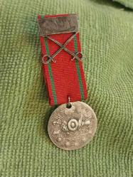 Kılıçlı Gümüş Liyakat Madalyası.. H.1332 M. 1916 Tarihli Gümüş Kılıçlı APARATI Olan Koleksiyonluk Liyakat Madalyası..  1890 tarihli Osmanlı dönemi Liyakat Madalyası. Üzerinde Osmanlı tuğrası, silah ve sancak motiflerinden oluşan devlet arması bulunan bu madalya, arka yüzünde Osmanlıca hat ile yazılmış metni ve altında 1308 (1890/1891) tarihini taşımaktadır. Osmanlı Devleti'nde liyakat ve hizmet karşılığı verilen bu madalyalar, devlet görevlileri ve askerî hizmet sahiplerine takdim edilirdi. Tarihi ve koleksiyon değeri yüksek olan bu eser, Osmanlı nişan ve madalya koleksiyonları için dikkat çekici nadir örneklerden biridir.