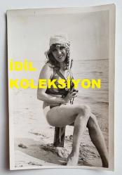 ŞANTÖZ AYLİN'İN (GÜLER) ORİJİNAL FOTOĞRAFI - 18 x 12 cm EBADINDA - ŞANTÖZ AYLİN, DENİZ KENARINDA KUMSALA OTURUP GÜLÜMSEYEREK KADRAJA POZ VERİRKEN ÇEKİLMİŞ BİR KARE