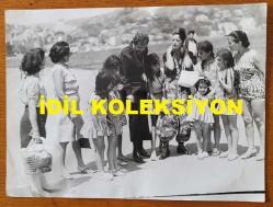 ŞARKICI BERKANT'IN ORİJİNAL BÜYÜK BOY FOTOĞRAFI - 24 x 18 cm EBADINDA - BERKANT, EŞİYLE BİRLİKTE SAHİLDE DOLAŞTIĞI SIRADA ETRAFINI SARAN KADIN ve ÇOCUK HAYRANLARIYLA AYNI KAREDEYKEN ÇEKİLMİŞ BİR FOTOĞRAF