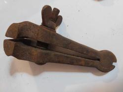 El Mengenesi. Osmanlı dönemine ait el yapımı bir el mengenesi (hand vice) koleksiyon parçasıdır.  Tarihi Değer: Genellikle dövme demirden üretilen bu tür aletler, antika ve koleksiyon değeri taşır.  Kullanım Alanı: Küçük parçaları tutmak, sıkıştırmak veya zımparalama/eğeleme işlemleri sırasında sabit tutmak için kullanılırdı.  Özellikleri: Görseldeki örnekte, parçayı sabitlemek için kullanılan klasik bir vida mekanizması ve yay bulunmaktadır.  Kullanım Amaçları: Takı yapımı, saat tamiri veya küçük metal parçaların işlenmesi gibi hassas işlerde yaygındı.